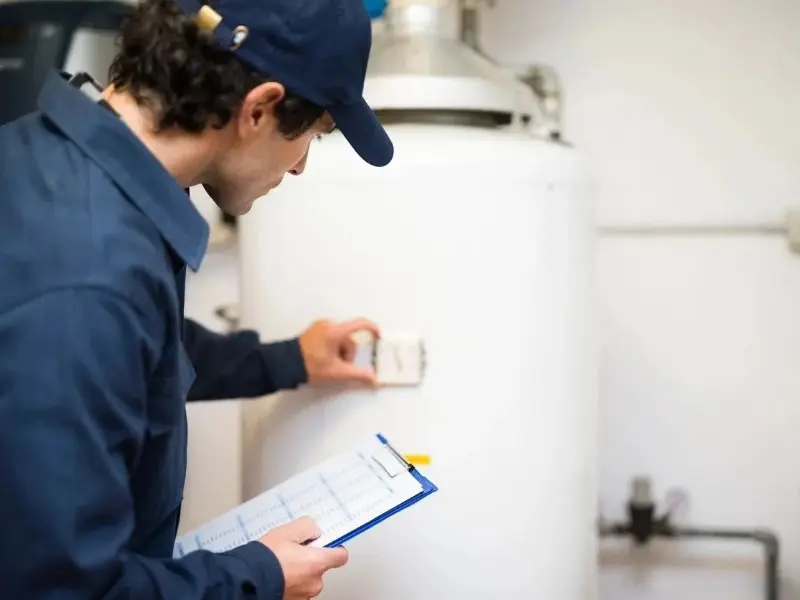 A man in blue shirt holding clipboard near water heater.