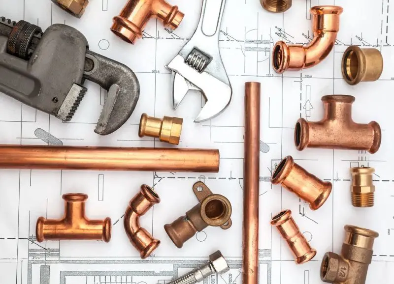 A bunch of copper pipes and tools on top of some plans